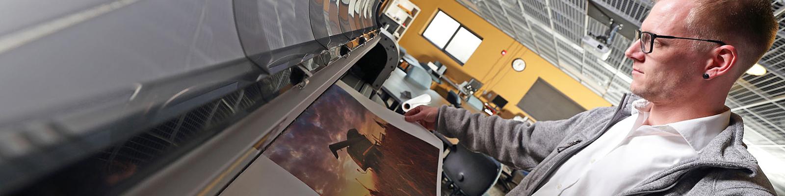Male student examining print on large scale printer